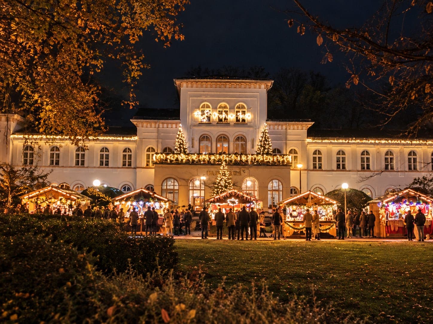 Der Bad Sodener Weihnachtsmarkt im Alten Kurpark: beleuchtete Holzhütten zwischen den Bäumen, Besucher zwischen den Ständen.
